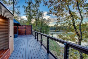 Eine Holzterrasse mit Geländer, die auf einen See und Bäume blickt.