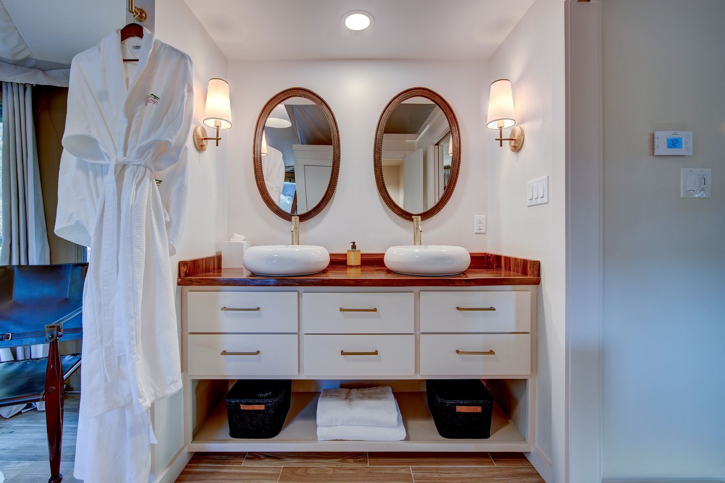 A hotel bathroom with two sinks, a robe rack, and a mirror.