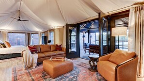 Une pièce aménagée comme une tente, avec un lit, un canapé, un pouf et un coin repas comprenant des chaises et une table.