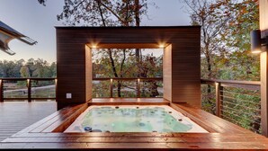 Ein Whirlpool auf einer Holzterrasse mit Blick auf Bäume und eine entfernte Landschaft.