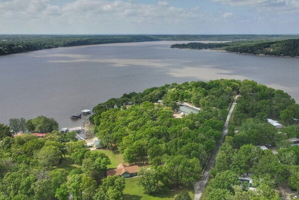 An aerial view of a lakeside property with dense greenery, a road, and a few buildings. - Hot Tub, Pool, Dock: 2 Cabins Lakeview Grand Lake (Grove)
