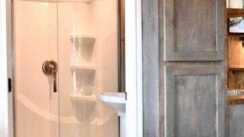 A room with a glass-enclosed shower, a white sink, and wooden cabinets.