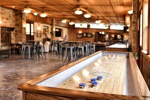 A bar area with a shuffleboard table, wooden bar stools, and hanging lights. - Texas Glamping Vacation Waterfront Cabin #18 in Marion, TX (Marion)