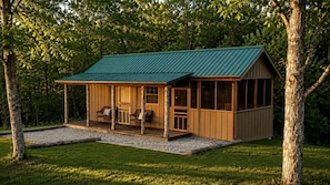 Eine Holzhütte mit einem grünen Dach, einer Veranda mit Sitzgelegenheiten und einem Kiesweg.