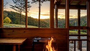 Una cabaña con interior de madera, una mesa, un hogar a leña y vistas a un paisaje boscoso.