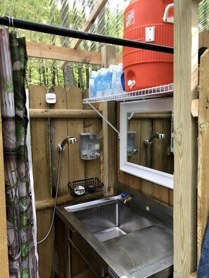 A compact outdoor kitchen with a sink, a water heater, and a red water tank.