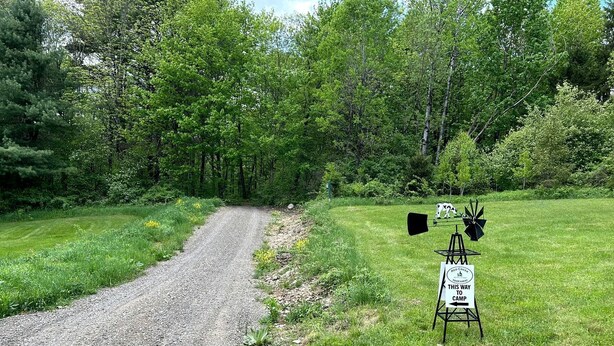 Ein Kiesweg führt zu einem Campingplatz, ein Schild weist den Weg zum Zeltplatz.