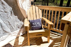 A wooden deck with a single Adirondack chair featuring a pillow with 'STAY awhile' text.
