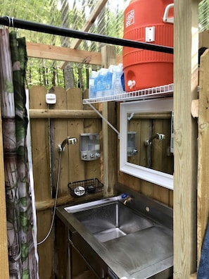 A compact outdoor kitchen with a sink, a water heater, and a red water tank.
