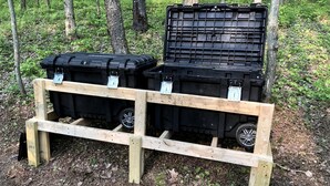 Zwei schwarze Aufbewahrungsboxen auf einer Holzpalette im Wald.