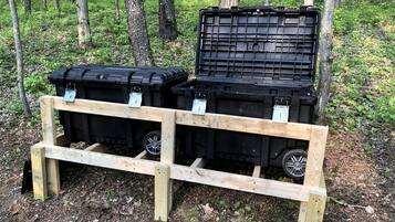 Two black storage bins on a wooden pallet in a forest.