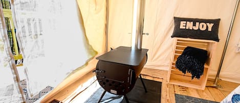 A tent with a portable stove, a 'ENJOY' sign, and a wooden bench.