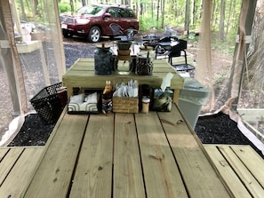 A wooden deck with a table, chairs, and various items like a basket, jars, and a trash can.
