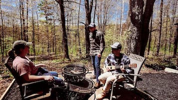 Un décor de forêt avec un foyer, des bancs et un guitariste.