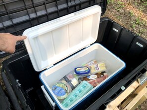 A portable cooler with a white lid, containing various food items and a blue container with eggs. - Luxurious Safari Tent in Cooperstown, NY - Perfect Glamping Spot for a Romantic Getaway (Cooperstown)