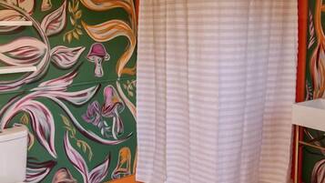 Une salle de bain avec des toilettes, une douche dotée d’un rideau à rayures et un mur orné d’un motif floral.