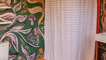 Un baño con inodoro, una ducha con cortina a rayas y una pared con estampado floral.