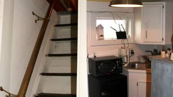 Un escalier avec une rampe en bois et des murs blancs, une cuisine avec des armoires blanches, un four à micro-ondes et un luminaire suspendu.