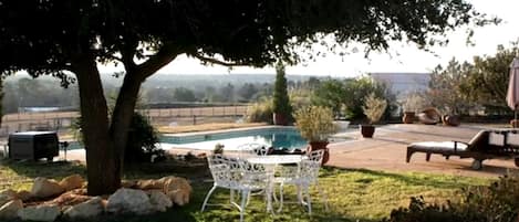 A backyard with a pool, a white table and chairs, a lounge chair, and a large tree.