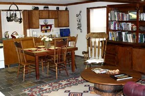 Uma sala de jantar com mesa e cadeiras de madeira, uma cozinha com armários de madeira e uma estante cheia de livros.