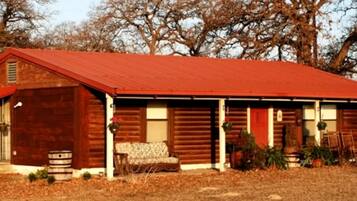 Une cabane en bois rustique avec un toit rouge, une véranda dotée d’un banc et un tonneau à l’extérieur.