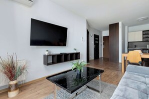 Ein modernes Wohnzimmer mit Fernseher, einem schwarzen Marmortisch, einer grauen Couch und einer Küche im Hintergrund.