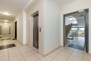 Ein moderner Flur mit Fliesenboden, einem Aufzug und einer Glastür, die auf einen Balkon führt.