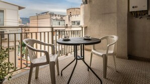Ein Balkon mit rundem Tisch, zwei Stühlen, einem Blumentopf und Blick auf Gebäude.