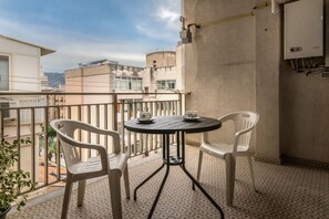 Ein Balkon mit rundem Tisch, zwei Stühlen, einem Blumentopf und Blick auf Gebäude.