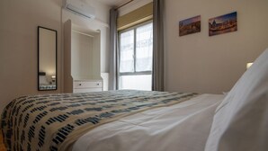 Ein Hotelzimmer mit Bett, einem Fenster mit Vorhängen, einem Spiegel und zwei Wandbildern.