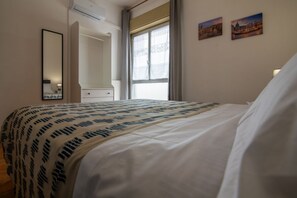 Ein Hotelzimmer mit Bett, einem Fenster mit Vorhängen, einem Spiegel und zwei Wandbildern.