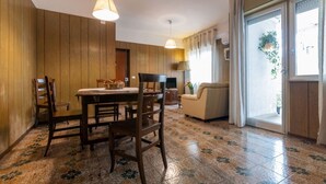 Ein Essbereich mit Holztisch und Stühlen, einer Couch und einem großen Fenster mit Vorhängen.