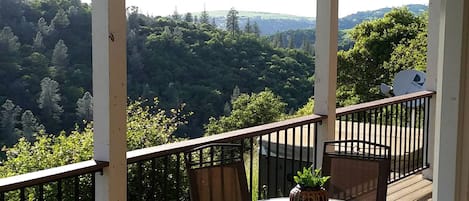 A balcony with a table and chairs, overlooking a forested landscape.