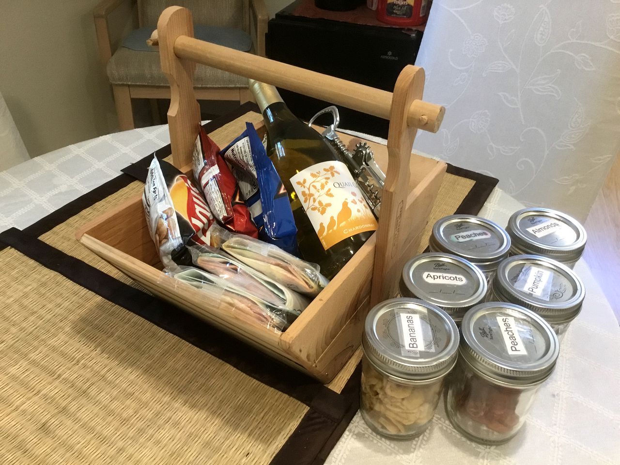 A wooden crate with a bottle, packaged food, and jars labeled with various fruits.