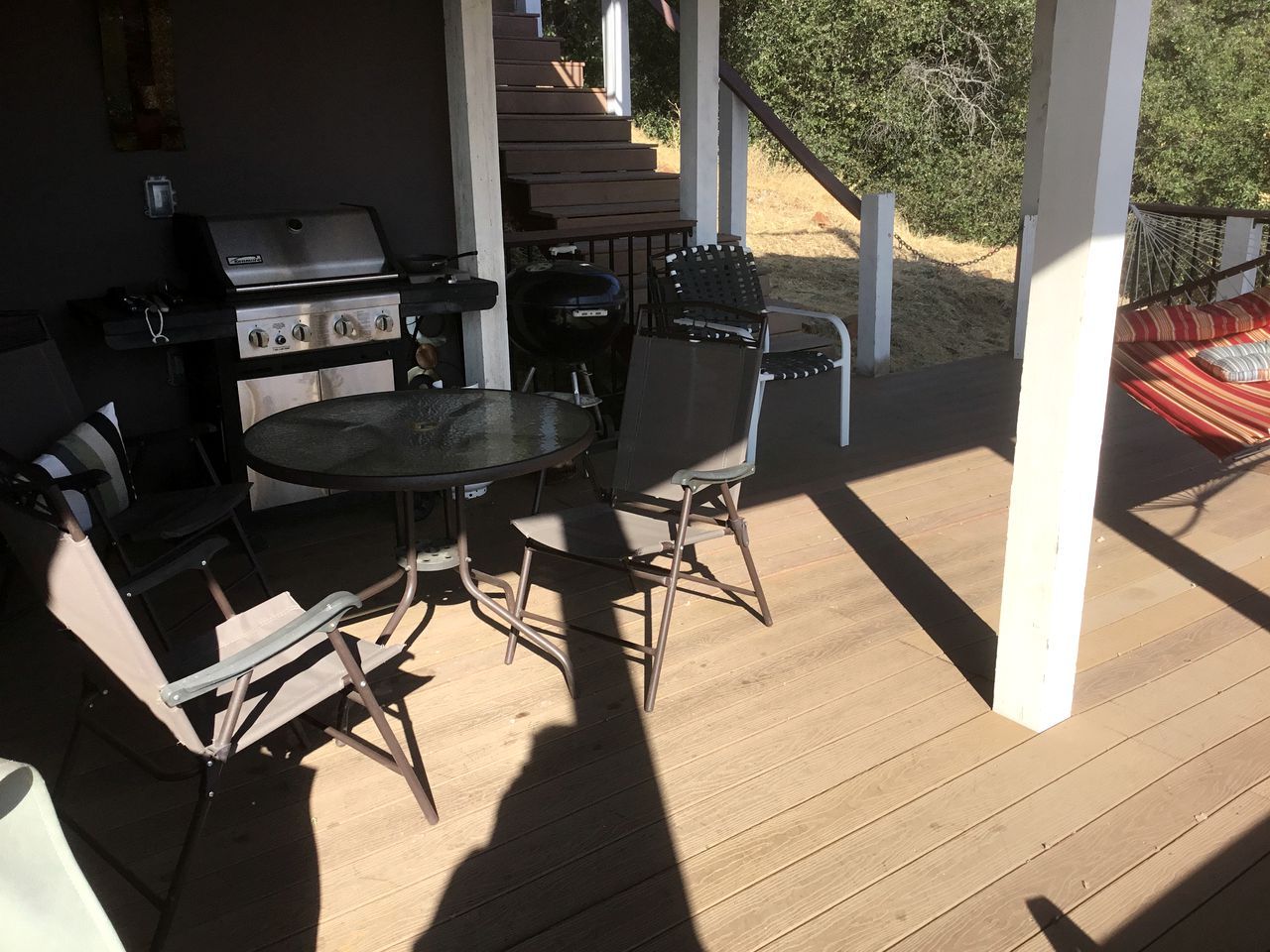 An outdoor patio with a grill, folding chairs, and a table.