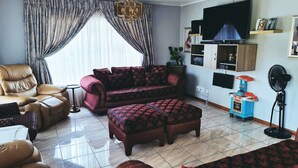 Una sala de estar con sofá, reposapiés y sillones, televisor y ventilador.