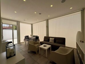 Ein modernes Wohnzimmer mit einer Couch, zwei Sesseln, einem kleinen Tisch und einem Esstisch mit Stühlen.