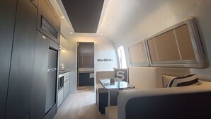 Un interior moderno y funcional con kitchenette, un pequeño comedor y una cama con cabecera.