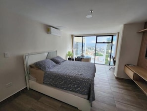 A bedroom with a bed, a window, and a view of the city.