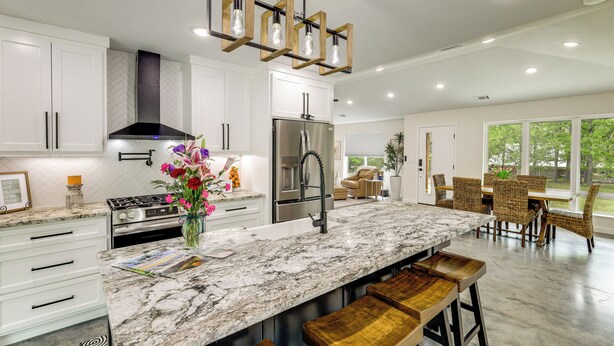 A modern kitchen with white cabinets, a marble countertop, stainless steel appliances, and wooden bar stools. - Modern-Style Home w/ Patio, Near Greers Ferry Lake (Heber Springs)