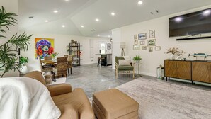 A spacious living area with a sofa, ottoman, and a dining table with chairs. There is a TV mounted on the wall and a bookshelf. - Modern-Style Home w/ Patio, Near Greers Ferry Lake (Heber Springs)