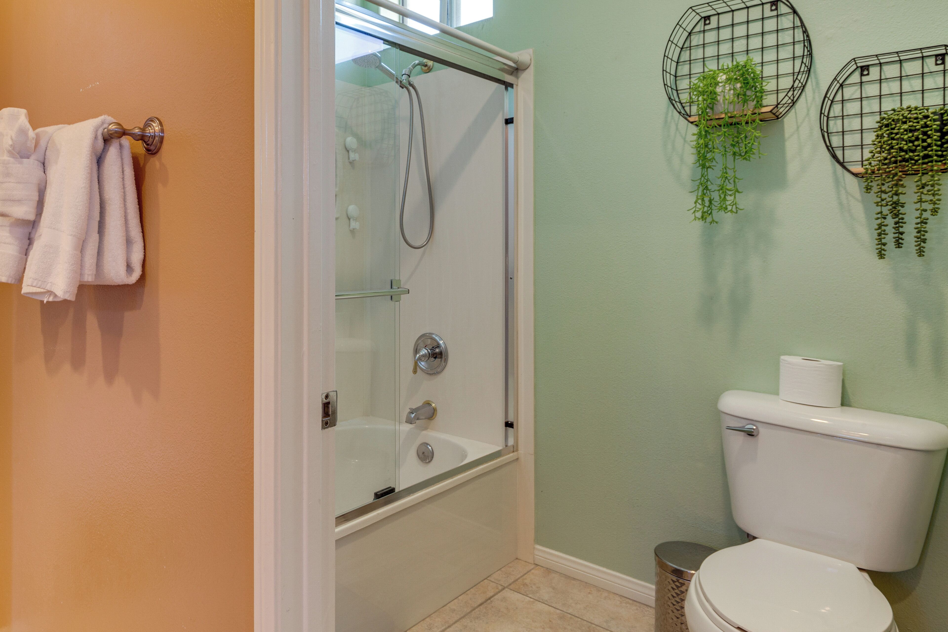 Un baño con ducha acristalada, inodoro y dos macetas colgantes con plantas.