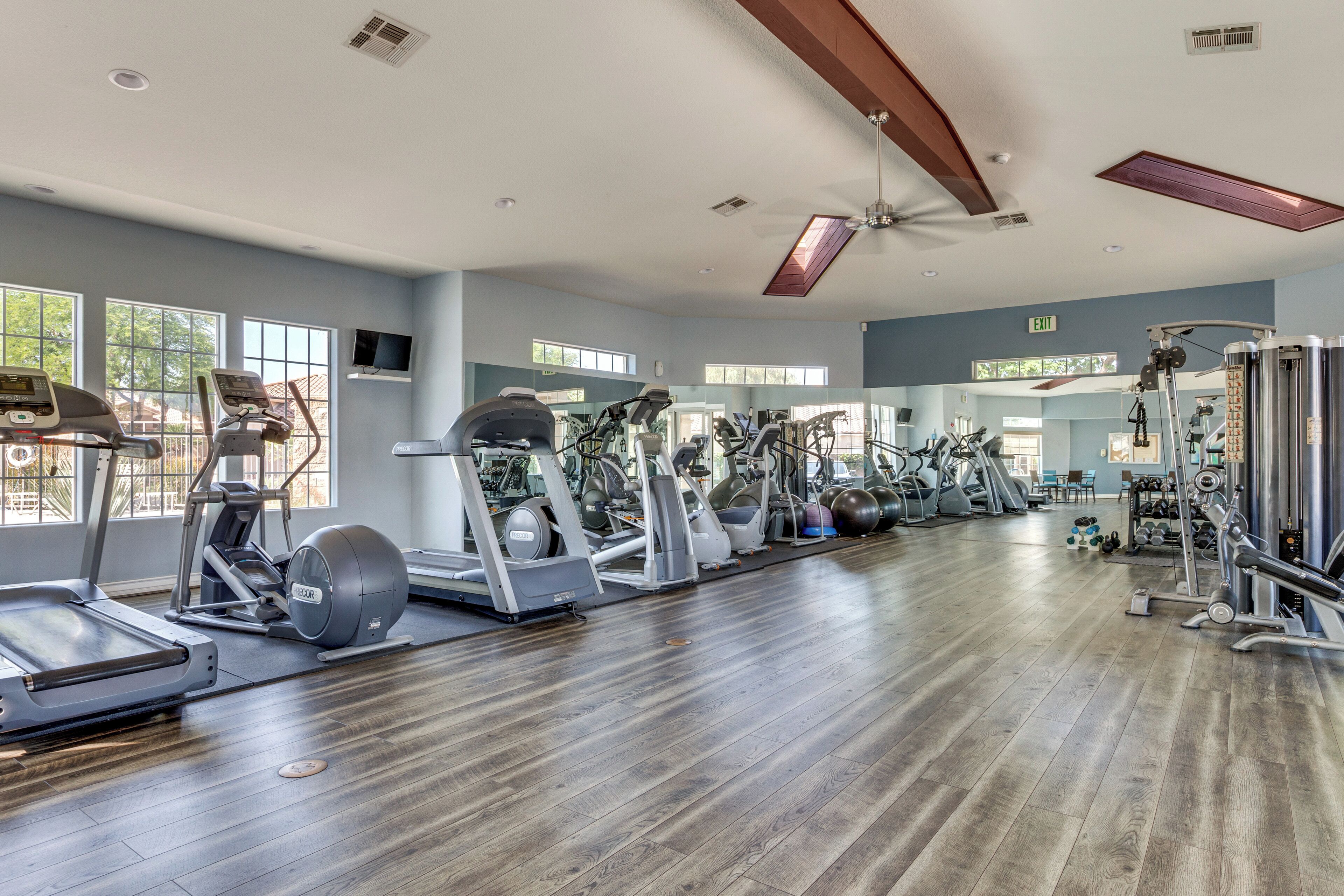 Een fitnessruimte met cardioapparaten, gewichthefapparatuur en een houten vloer.