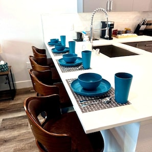 Une cuisine avec un plan de travail blanc, de la vaisselle bleue et des chaises en bois.