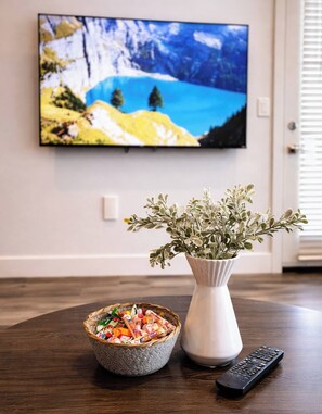 Ett matbord med en skål med snacks, en vas med gröna växter och en fjärrkontroll.