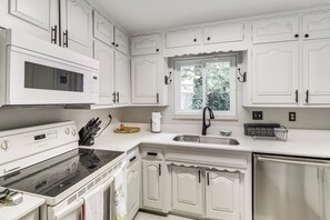 A kitchen with white cabinetry, a microwave, stove, sink, and a window with a view of greenery. - Walk to UNM! Quiet Extended Escape w/ Patio (Albuquerque)