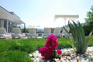 A pool area with lounge chairs, a white umbrella, and a large aloe plant. - Fethiye Göcek Villa BegonVilla (Fethiye)