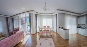 A spacious living room with a large window, a dining area with a table and chairs, and a kitchen area. - Fethiye Göcek Villa BegonVilla (Fethiye)