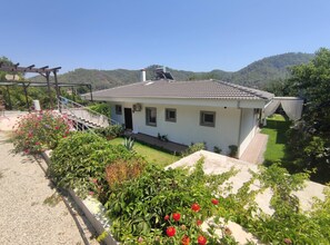 A two-story house with a tiled roof, a front porch, and a garden with various plants and flowers. - Fethiye Göcek Villa BegonVilla (Fethiye)