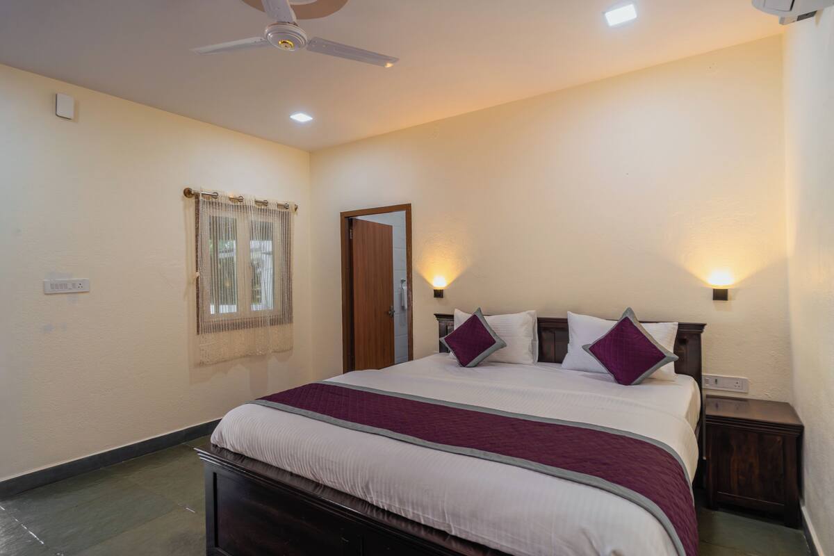 A hotel room with a bed, bedside tables, a ceiling fan, and a window with curtains.